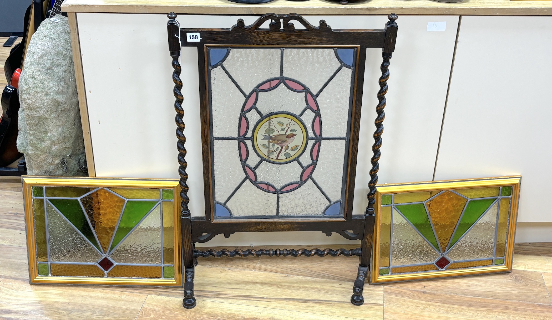 An early 20th century stained glass oak firescreen, height 84cm together with a pair of Art Deco style stained glass panels